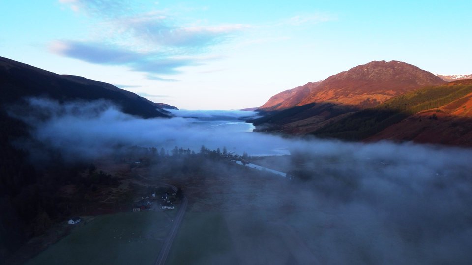 Morning mist fills a valley beneath sunlit mountain slopes.